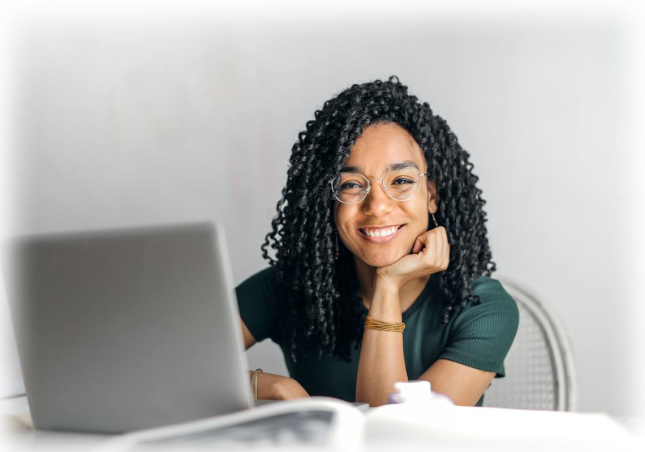 Image of a lady smiling at the camera while using her laptop.