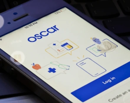 Tablet screen displaying Oscar health insurance app interface with login page and various healthcare service icons, representing digital access to modern health insurance benefits and member services