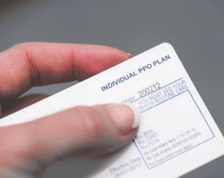 Hand holding Individual PPO Plan insurance card showing plan details and member information, representing physical proof of healthcare coverage and insurance benefits for medical services