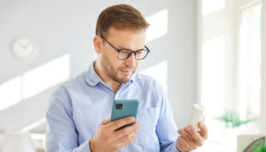 Man in glasses looking at smartphone in bright office environment, illustrating accessibility of online anxiety screening tools