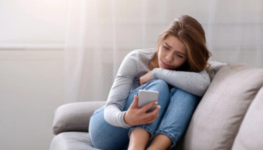 Woman sitting on couch holding phone, creating a comfortable space for taking a mental health assessment