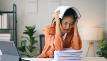 Woman in orange shirt holding her head with both hands appearing distressed, representing the emotional state that might prompt someone to seek panic disorder screening