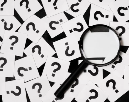 Magnifying glass hovering over scattered paper pieces with question marks, representing the search for answers and information about depression screening and mental health assessments