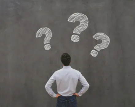 Person in white shirt standing with hands on hips facing wall with three large chalk question marks, symbolizing contemplation and seeking answers about mental health concerns