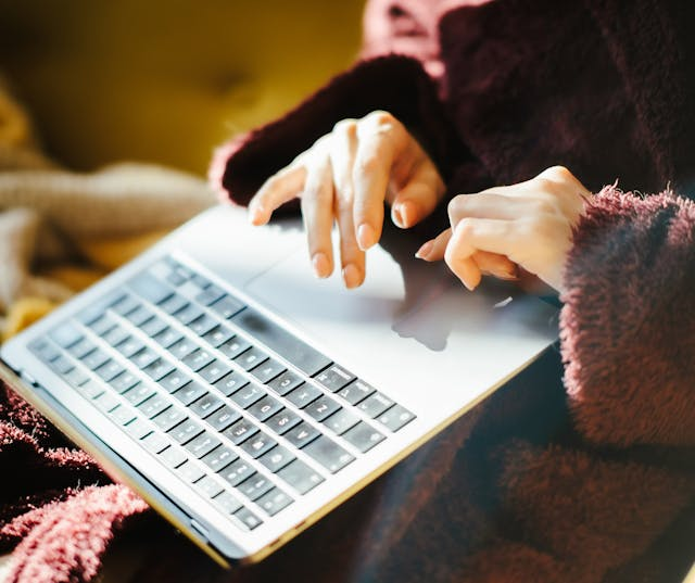 Close-up view of person's hands actively typing on laptop keyboard with trackpad visible, captured from above during online research